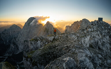 Obraz premium Hiker silhouette standing on rocky summit above misty valley. Nature daybreak background. Strong sun.