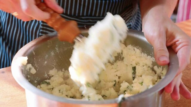Mashing Potatoes In A Pan On The Home Kitchen. Close-up of cook pounds potatoes with herbs.