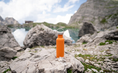 Close-up orange coloured water bottle in the mountains. Copy space. Zero waste, no plastic,...