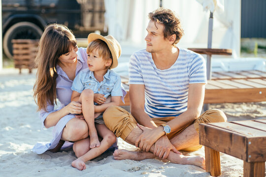 Photo portrait of happy family of three sitting on sand on summer vacation.