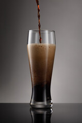 Glass of fresh and cold beer on a gray background. Detail of dark beer with overflowing foam head....