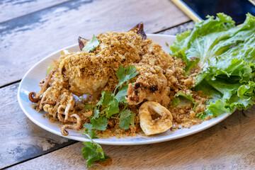 Fried squid with galic and coriander on top in white dish on wood table, ready to eat.