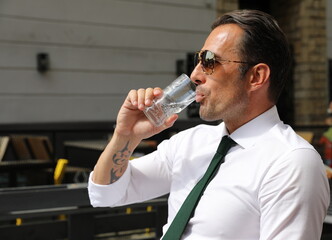 Fototapeta na wymiar Bardzo przystojny, elegancki mężczyzna w białej koszuli i zielonym krawacie i okularach przeciwsłonecznych.