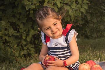 Little girl sitting on the grass holding an apple