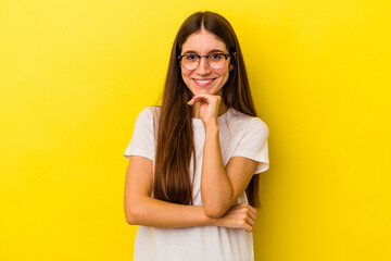 Young caucasian woman isolated on yellow background smiling happy and confident, touching chin with hand.