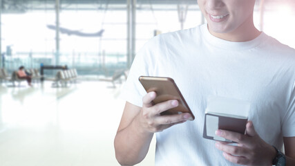 Smiling happy Young man waiting for flight and using mobile phone at the airport with passport.