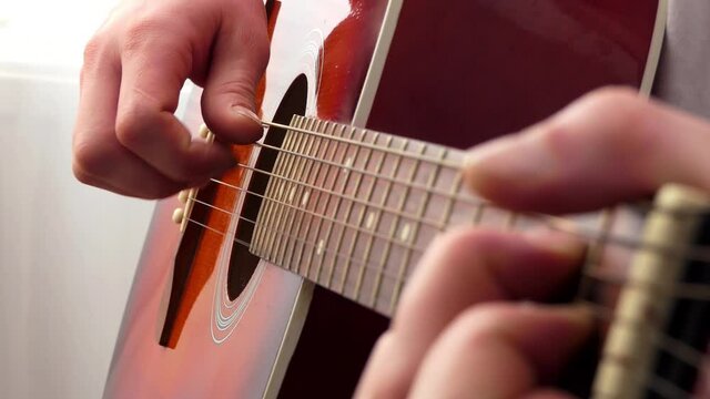 Closeup man fingers holding mediator in recording studio. Man hand playing guitar in white room.  Guitar strings close up.
