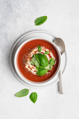 Tomato soup with strachatella cheese and basil. Bowl of fresh vegetable soup on white stone background