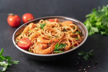 Spaghetti with shrimps in tomato cream sauce on black background