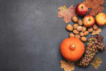 Autumn vegetables, fruits, nuts and dry leaves on black background. Fall background with copy space