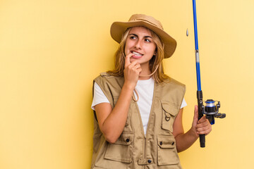 Young caucasian blonde fisherwoman holding a rod isolated on yellow background  relaxed thinking about something looking at a copy space.