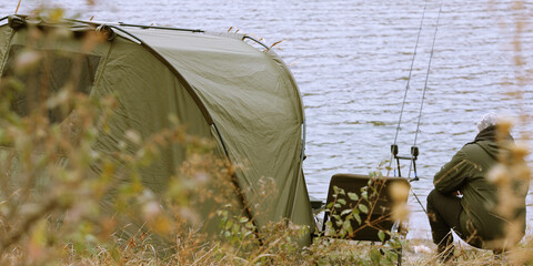 carp green tent by the lake with fishing rods and fisherman