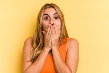 Young caucasian blonde woman isolated on yellow background  shocked covering mouth with hands.