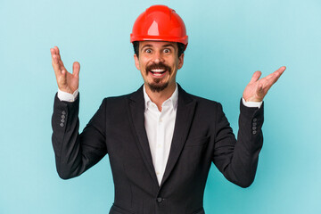 Young architect caucasian man isolated on blue background receiving a pleasant surprise, excited and raising hands.