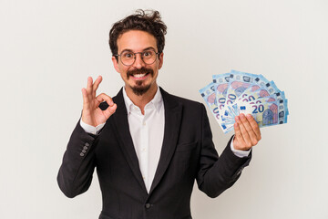 Young caucasian man holding banknotes isolated on white background cheerful and confident showing ok gesture.