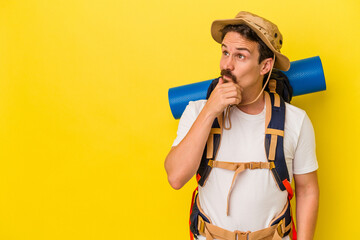 Young caucasian hiker man isolated on yellow background looking sideways with doubtful and skeptical expression.