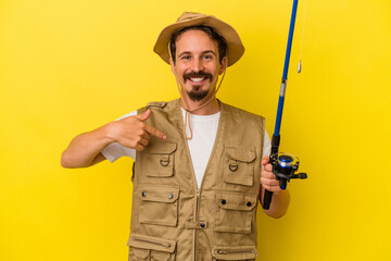 Young caucasian fisherman holding rod isolated on yellow background person pointing by hand to a shirt copy space, proud and confident