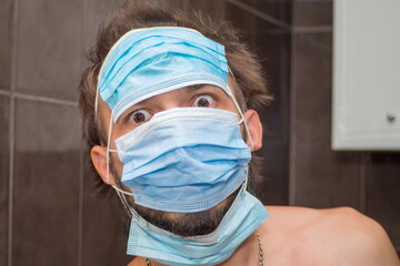 A surprised young bearded man wearing three medical masks at once