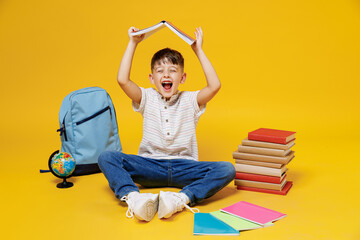 Young school boy 5-6 years old in t-shirt casual clothes sit holding book over head like roof...