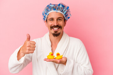Young caucasian man going to the shower with rubber ducks isolated on pink background smiling and...