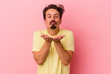 Young caucasian man isolated on pink background folding lips and holding palms to send air kiss.