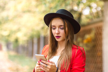 Close up portrait of young Woman in black hat and red jaket using mobile phone on city street..
