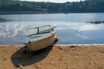 An old metal motor boat lies on the shore of the lake. You can see the opposite shore with a forest...
