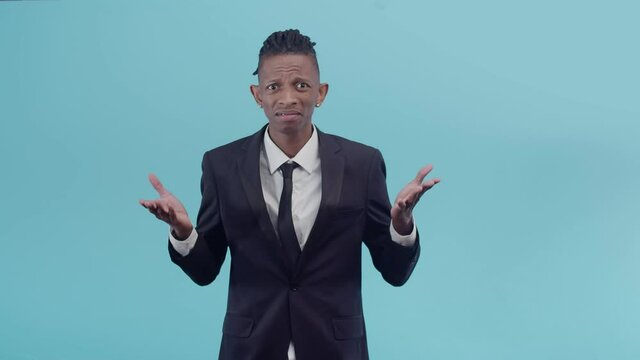 Disgruntled black male businessman indignantly makes a gesture with a crazy hand in the studio on blue background.