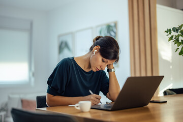 Portrait of a overworked woman writing notes, at home office.