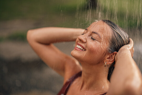 People, summer and happiness concept. Close-up image of a happy woman under outdoors shower.