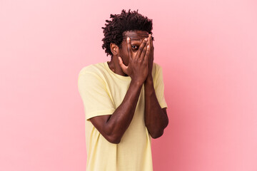 Young african american man isolated on pink background blink through fingers frightened and nervous.