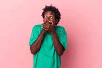 Young african american man isolated on pink background thoughtful looking to a copy space covering mouth with hand.