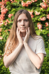 Fototapeta premium Close-up portrait of beautiful caucasian woman with long blond hair in the park. Natural beauty, make up free. Pink flowers on the background. 