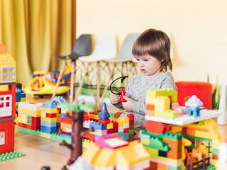 Toddler boy is playing in kidsroom with colorful constructor. Educational toy block in his hands. Kid is busy with toy bricks.