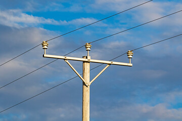 Old wooden power pole with wires on insulators against clouded sky