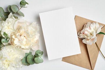 Obraz na płótnie Canvas Wedding invitation or greeting card mockup with envelope and white peony flowers with eucalyptus twigs