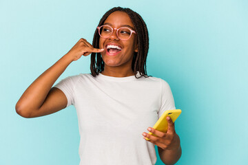 Young African American woman holding a mobile phone isolated on blue background  showing a mobile phone call gesture with fingers.