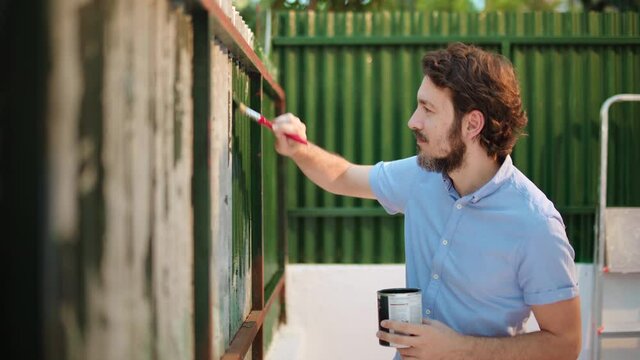 DIY Man paints an old metal fence wall into green