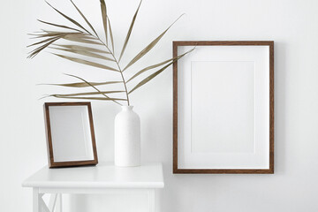 Two portrait wooden passepartout frames mockup on white wall for artwork, photo or print presentation. Minimalist interior design with vase and palm leaf.