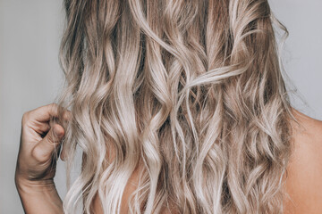 Close-up of a young blonde woman standing with her back with the wavy hair touches her hair with...