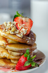 Pancakes stacked with bananas, strawberries and nuts, topped with chocolate and strawberry sauce