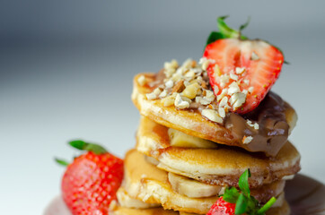 Pancakes stacked with bananas, strawberries and nuts, topped with chocolate and strawberry sauce