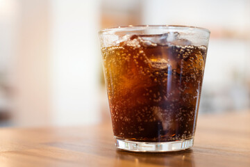 Soft drink with ice in a glass on a walnut colored table