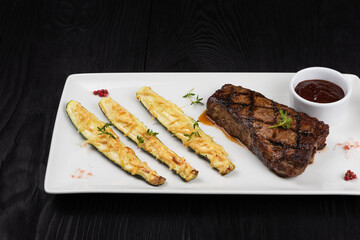 Grilled black angus strip loin steak New York with zucchini on white plate on black wooden background with