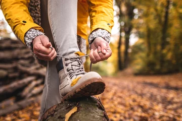 Fotobehang Woman tying shoelace on her hiking boot. Tourist is getting ready for autumn hike at woodland trekking trail © encierro