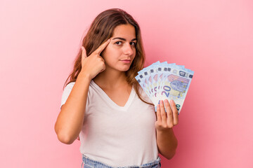 Young caucasian woman holding bills isolated on pink background  pointing temple with finger, thinking, focused on a task.
