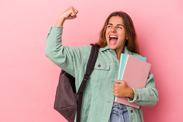 Young caucasian student woman holding books isolated on pink background  raising fist after a...