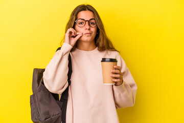 Young caucasian student woman holding coffee isolated on yellow background  with fingers on lips keeping a secret.