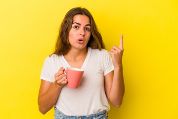 Young caucasian woman holding a mug isolated on yellow background  having some great idea, concept of creativity.