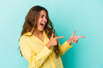 Young caucasian woman isolated on blue background  points with thumb finger away, laughing and carefree.